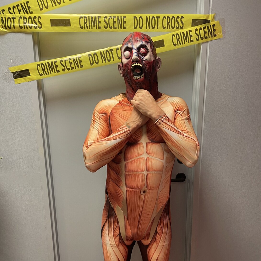 Employee with a monster suit on. Standing in front of a door blocked with tape saying crime scene.